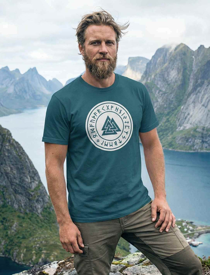 Mann trägt blaugrünes Valknut Organic Shirt – Zeichen Odins mit Runenkreis und Valknut Symbol in nordischer Landschaft