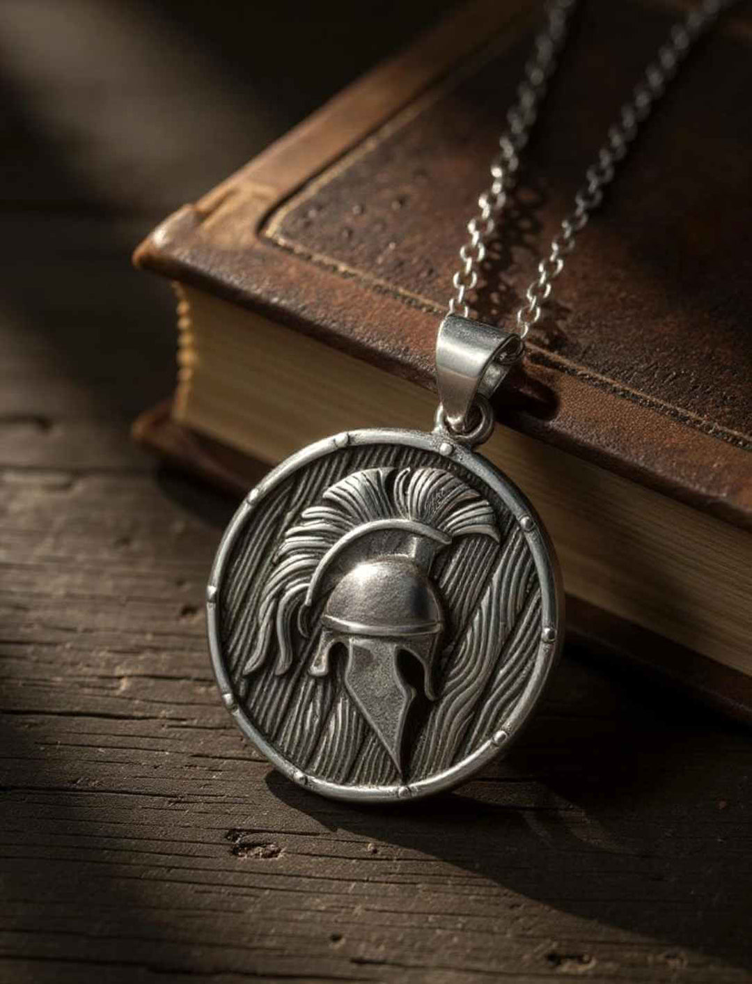 Spartanischer Helm-Anhänger aus Edelstahl auf einer alten Ledermappe, mystisch ausgeleuchtet mit Fokus auf historischer Symbolkraft.