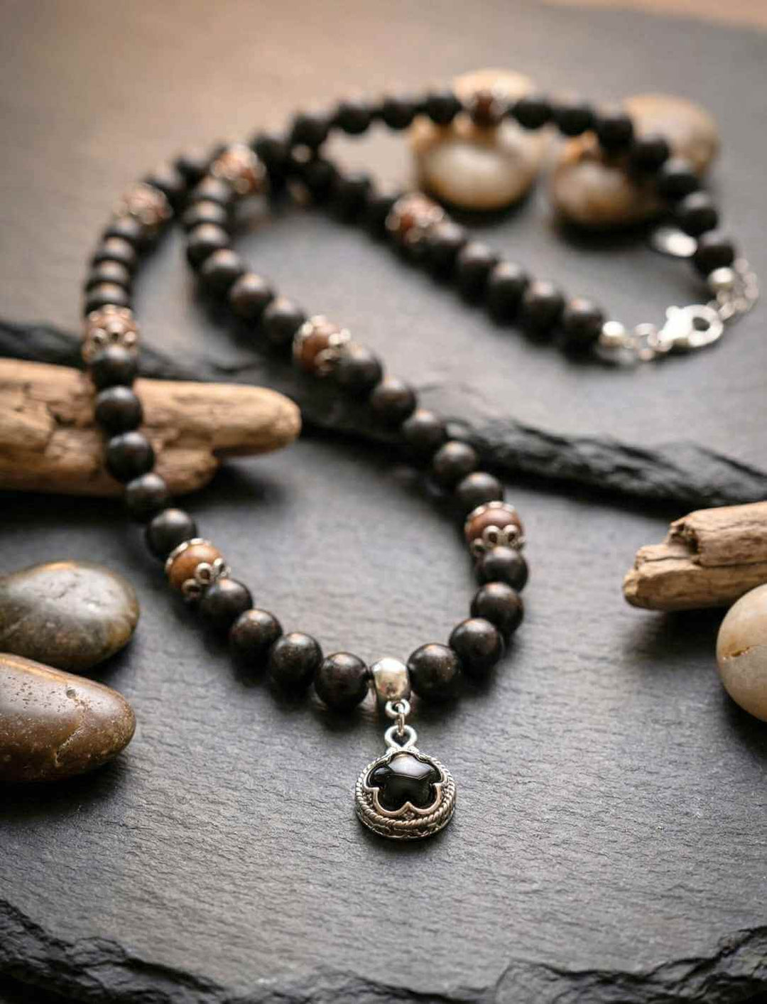 Waldhüter von Gotland – Schutzamulett aus Holzperlen mit Onyx Anhänger, liegend auf dunklem Stein mit Naturdekoration