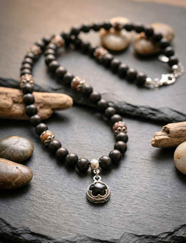 Waldhüter von Gotland – Schutzamulett aus Holzperlen mit Onyx Anhänger, liegend auf dunklem Stein mit Naturdekoration