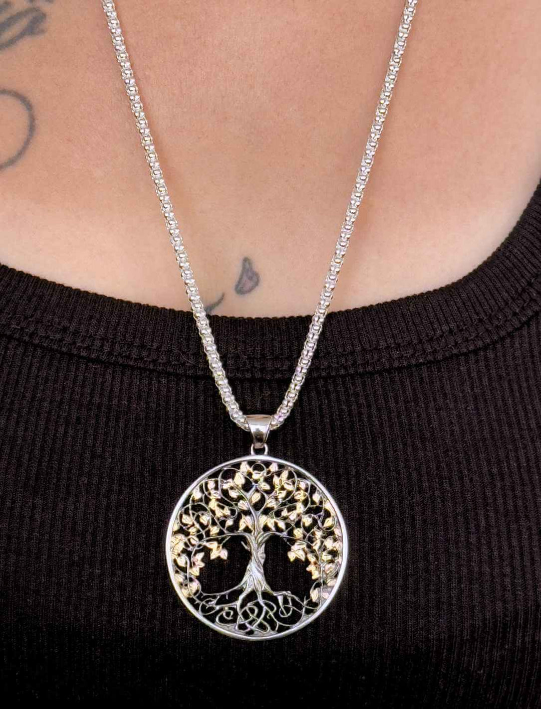 Model trägt Lebensbaum-Medaillon aus Silber, teilvergoldet und schwarz paltiniert, mit Silberkette im Popcorndesign.