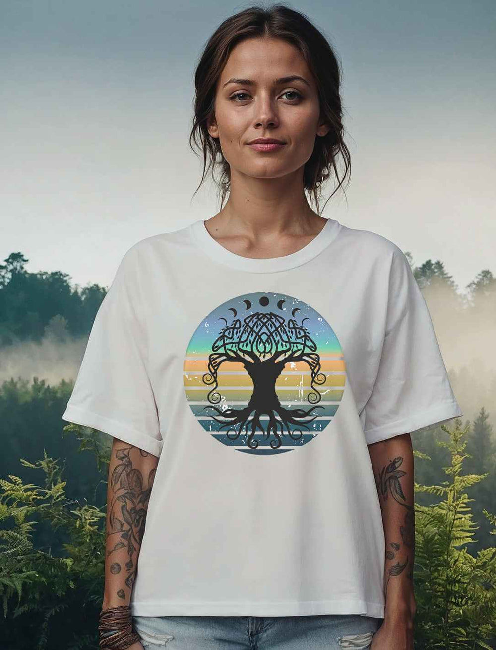 Frau in weißem Relaxed T-Shirt mit dem Yggdrasil-Motiv vor nebelverhangener Waldlandschaft bei Morgendämmerung.