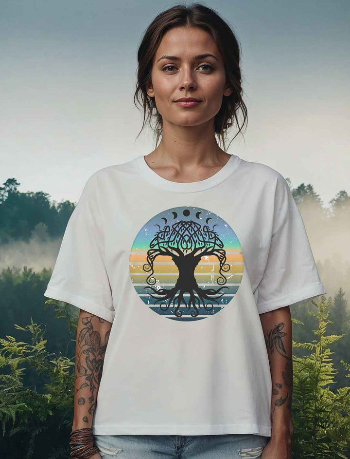 Frau in weißem Relaxed T-Shirt mit dem Yggdrasil-Motiv vor nebelverhangener Waldlandschaft bei Morgendämmerung.