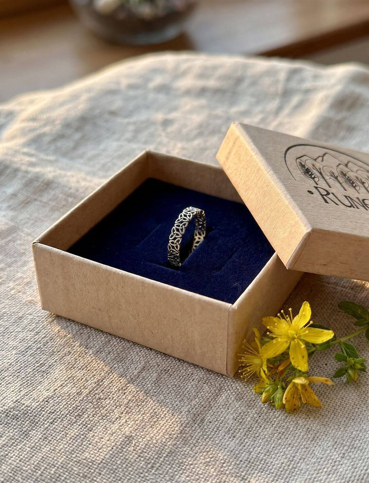 Triquetra Bandring in der Runental Geschenkbox aus Karton mit blauem Samt, daneben ein Zweig Johanniskraut