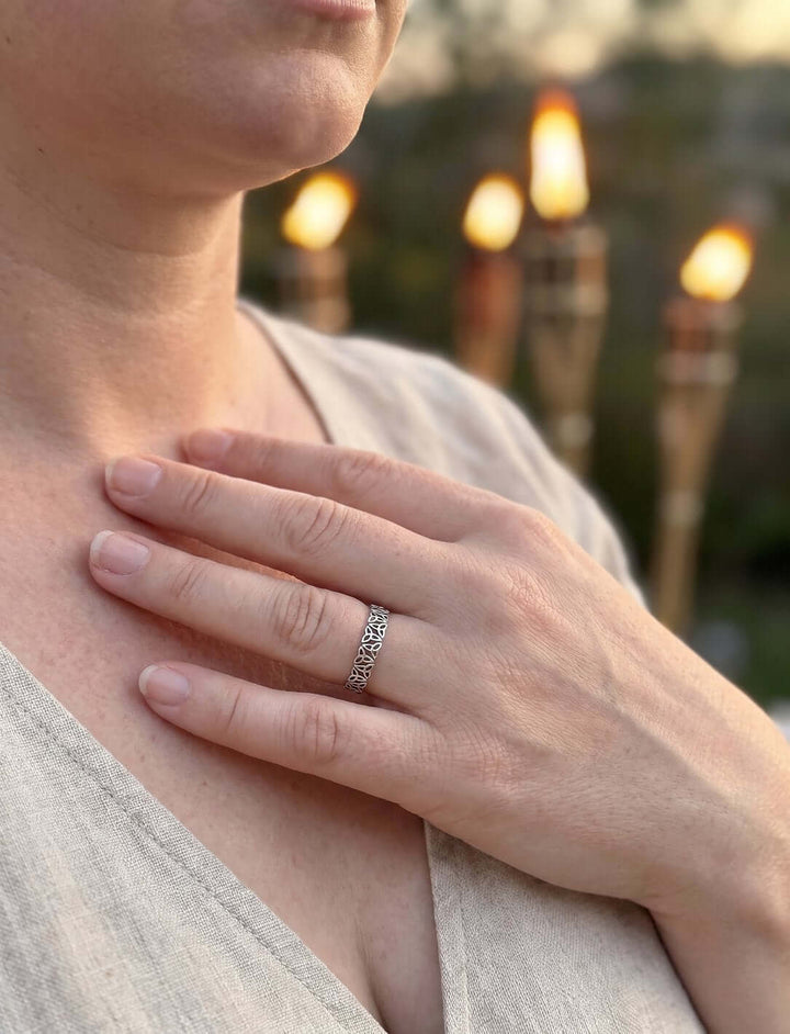Frau im Leinenkleid mit der Hand am Schlüsselbein, am Finger ein Silberring aus Dreifaltigkeitsknoten, Fackeln im Hintergrund
