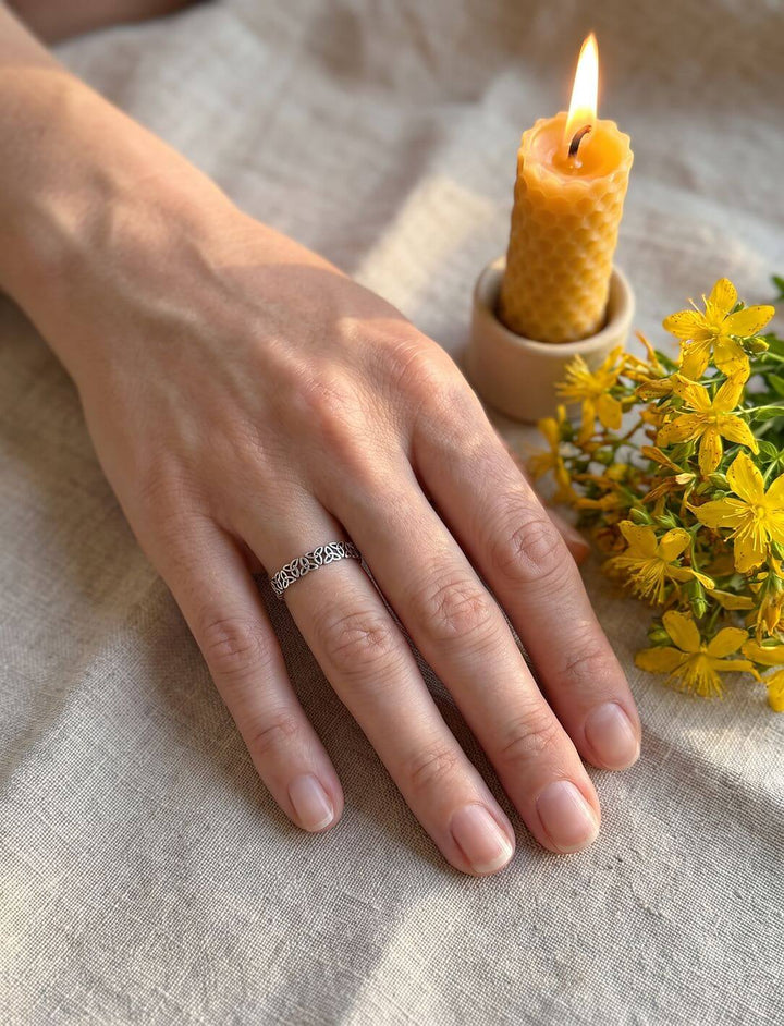 Frauenhand mit schmalem Triquetra Ring aus Silber am Ringfinger, auf Leinen neben Bienenwachskerze und Johanniskraut