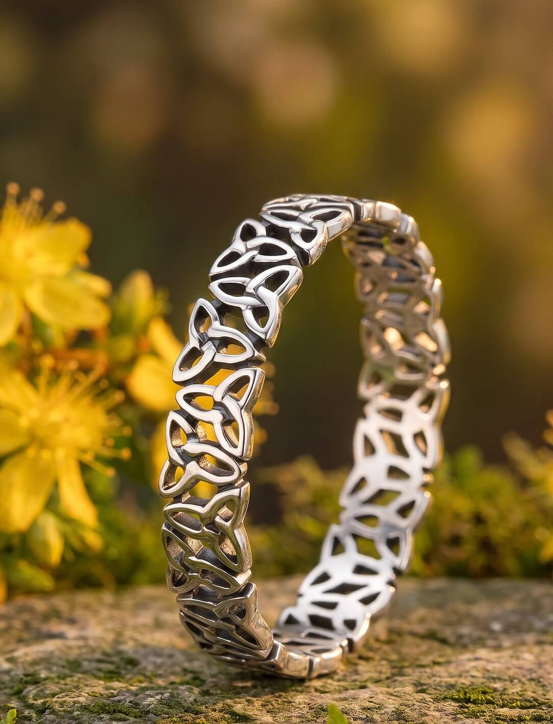 Áines Kreis: keltischer Knoten Ring aus 925 Silber auf moosigem Stein vor blühendem Johanniskraut im Abendlicht