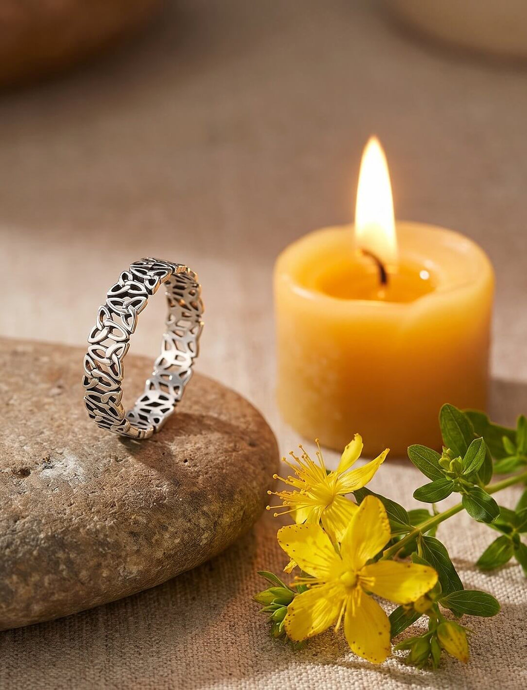 Durchbrochener Silberring mit keltischen Knoten steht auf einem Flussstein neben einer brennenden Bienenwachskerze