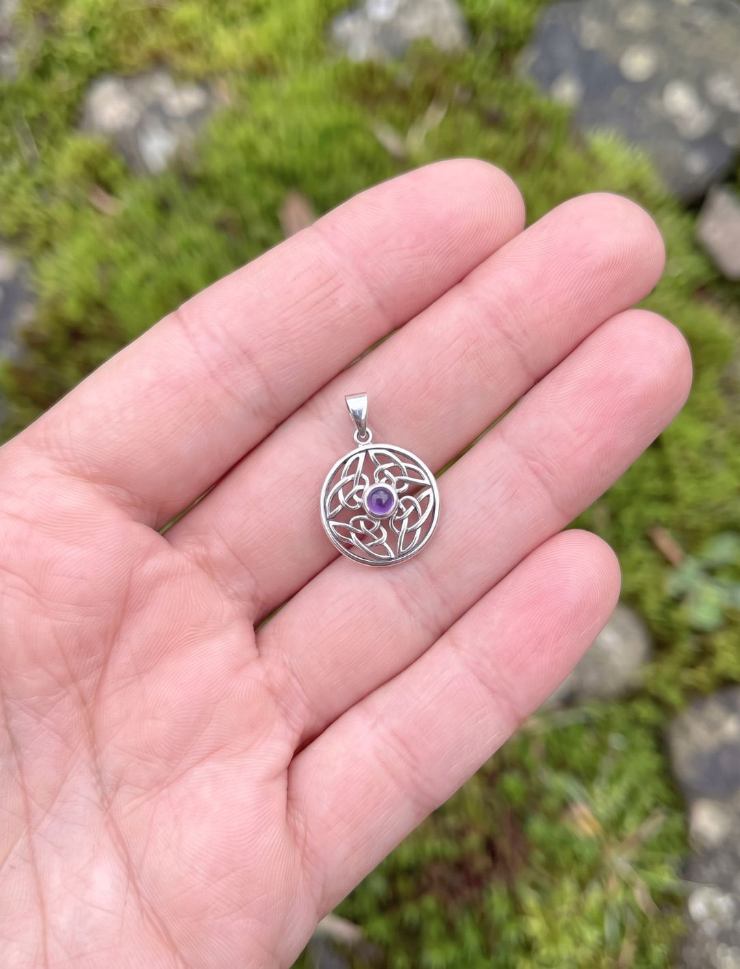 Silberner Knotenanhänger mit Amethyst in einer offenen Hand als Größenvergleich