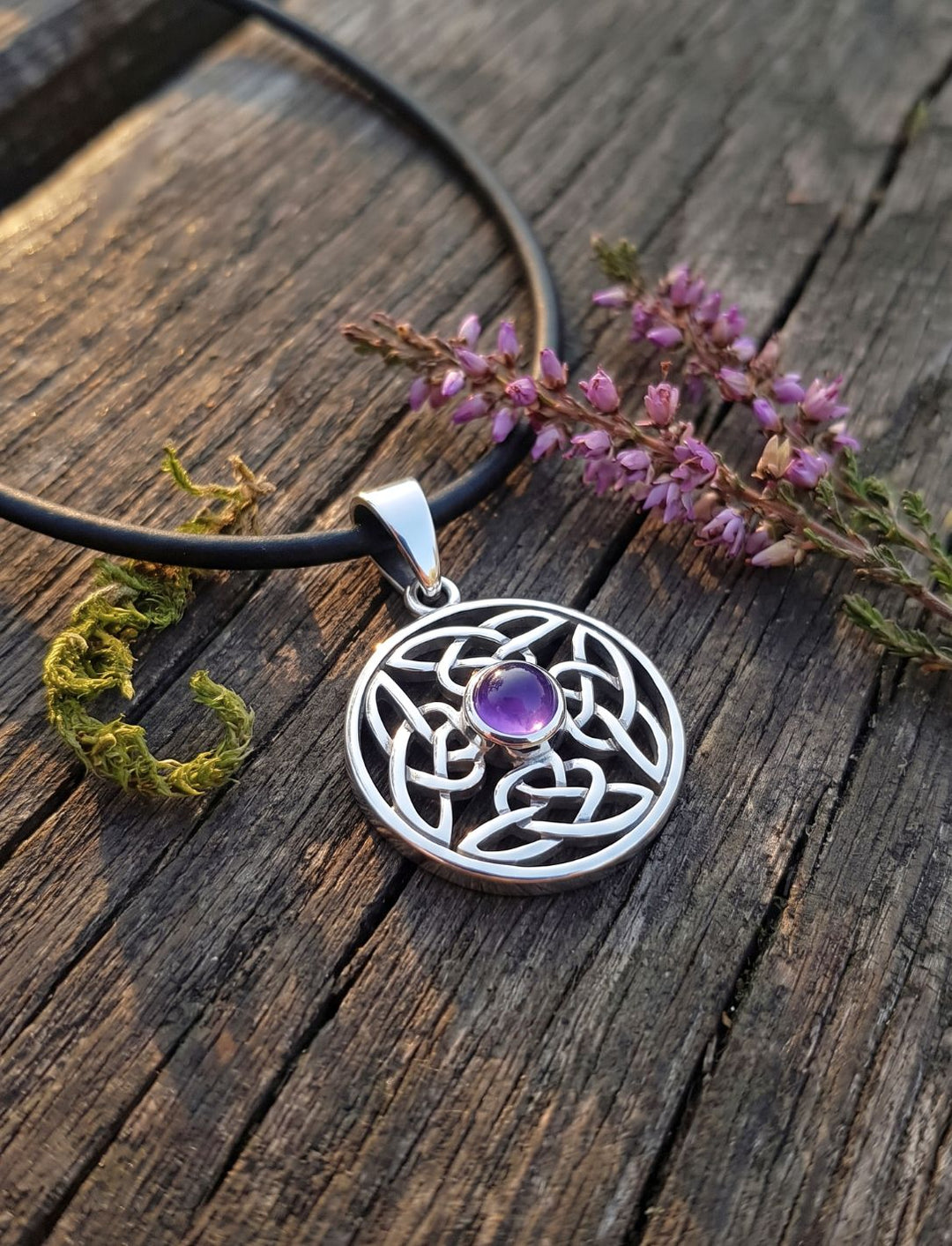 Amethyst Anhänger an schwarzer Lederkordel auf verwittertem Holz mit Heidezweig und Moos