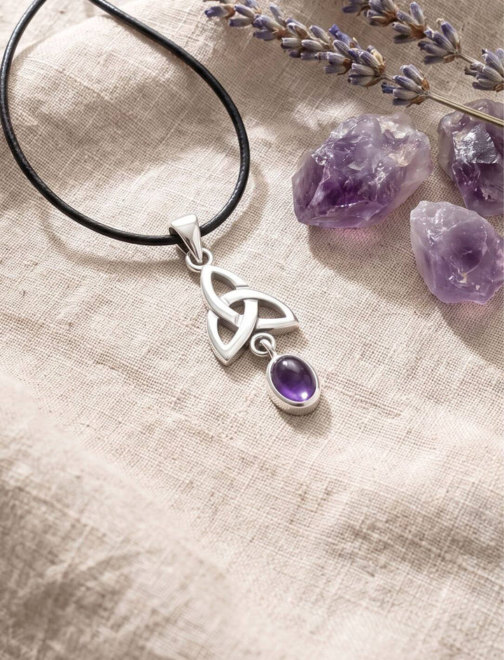 Keltischer Triquetra Anhänger mit Amethyst am Lederband neben Rohamethyst-Stufen und Lavendel