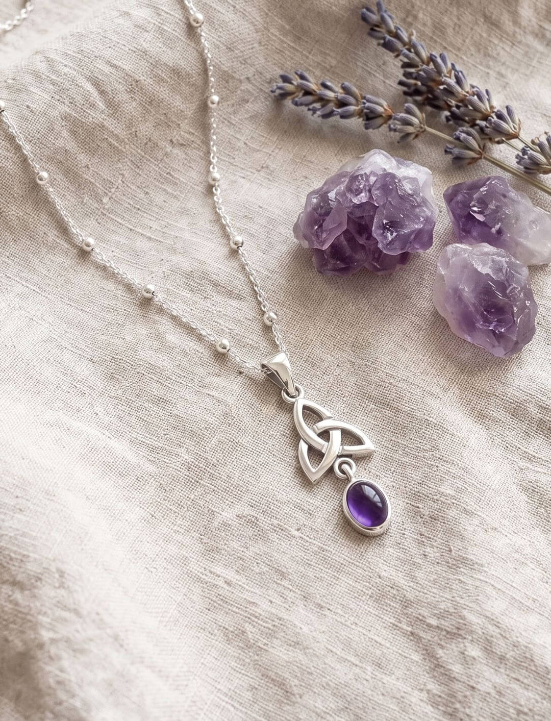 Silberanhänger mit Amethyst an Kugelkette neben Rohamethyst und getrocknetem Lavendel auf Leinen