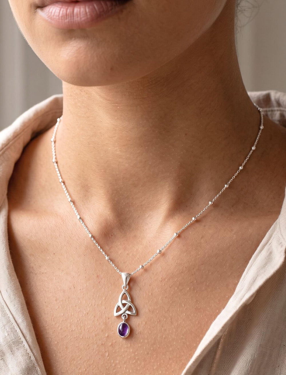 Frau trägt filigranen Silberanhänger mit Amethyst an feiner Kugelkette zu offener heller Bluse