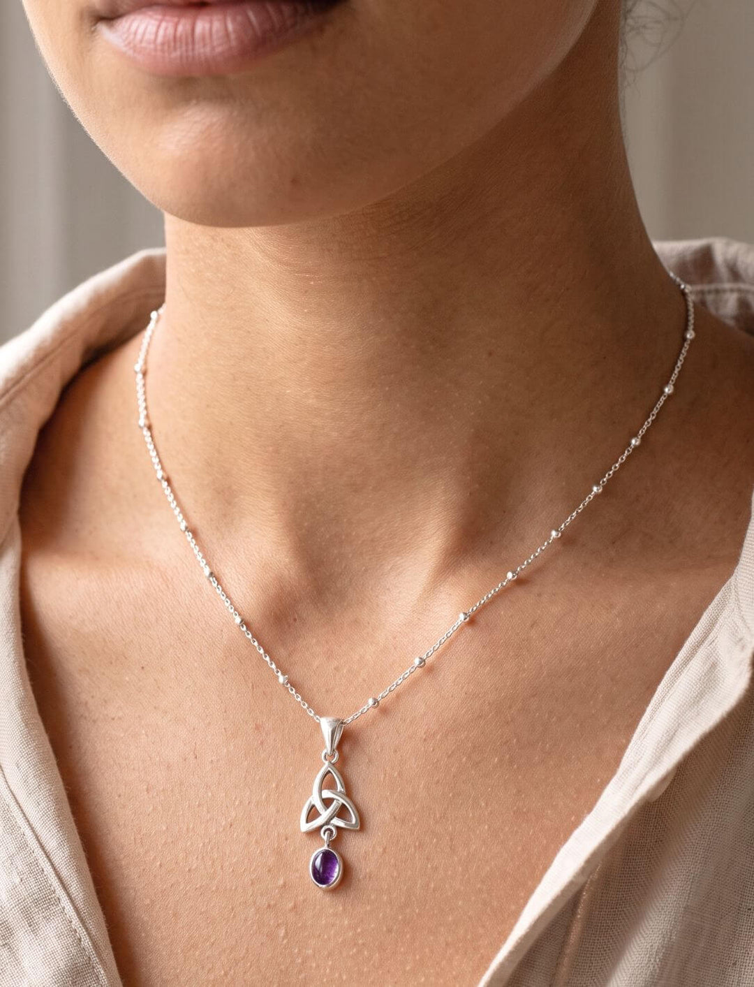 Frau trägt filigranen Silberanhänger mit Amethyst an feiner Kugelkette zu offener heller Bluse