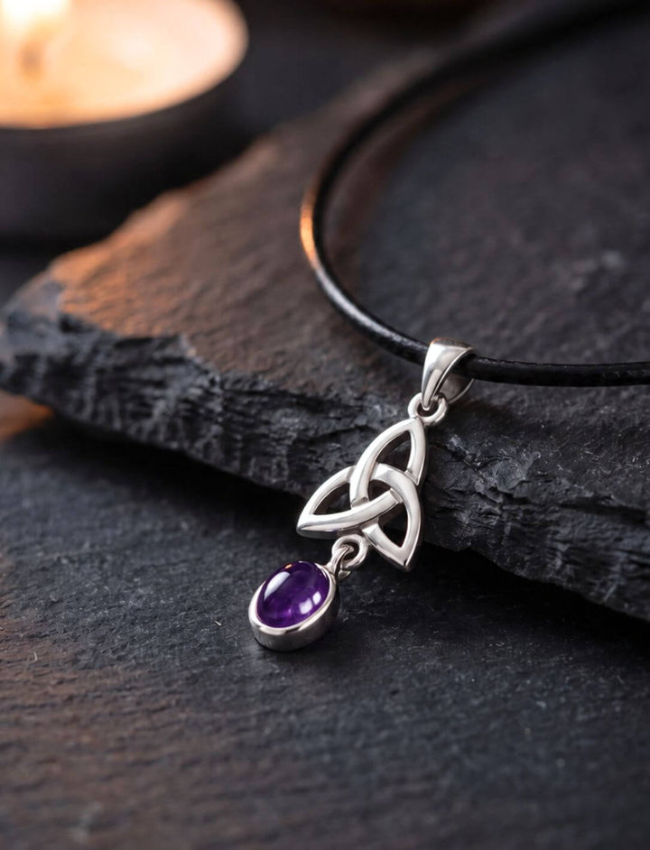 Amethyst Anhänger aus Silber mit keltischem Triquetra-Knoten auf dunklem Schiefer im Kerzenlicht