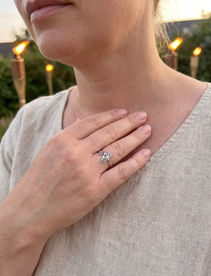 Frau im Leinenkleid mit der Hand am Schlüsselbein trägt einen Triskel Ring aus Silber, Fackeln im Abendlicht