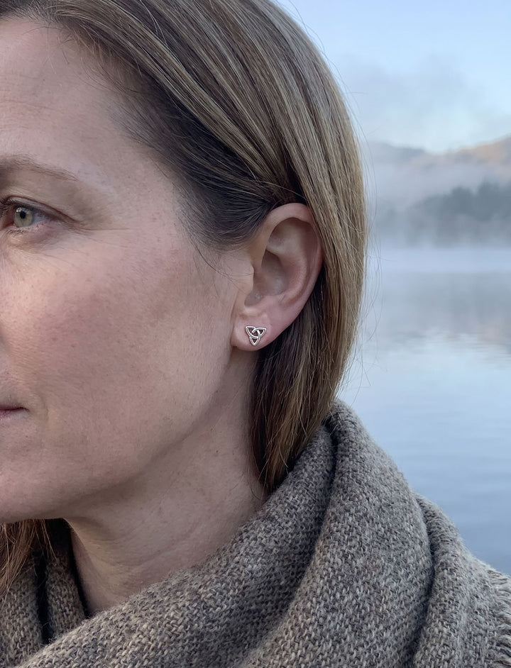 Kleiner keltischer Knoten Ohrstecker aus Silber am Ohr einer Frau mit Wollschal am See im Morgennebel