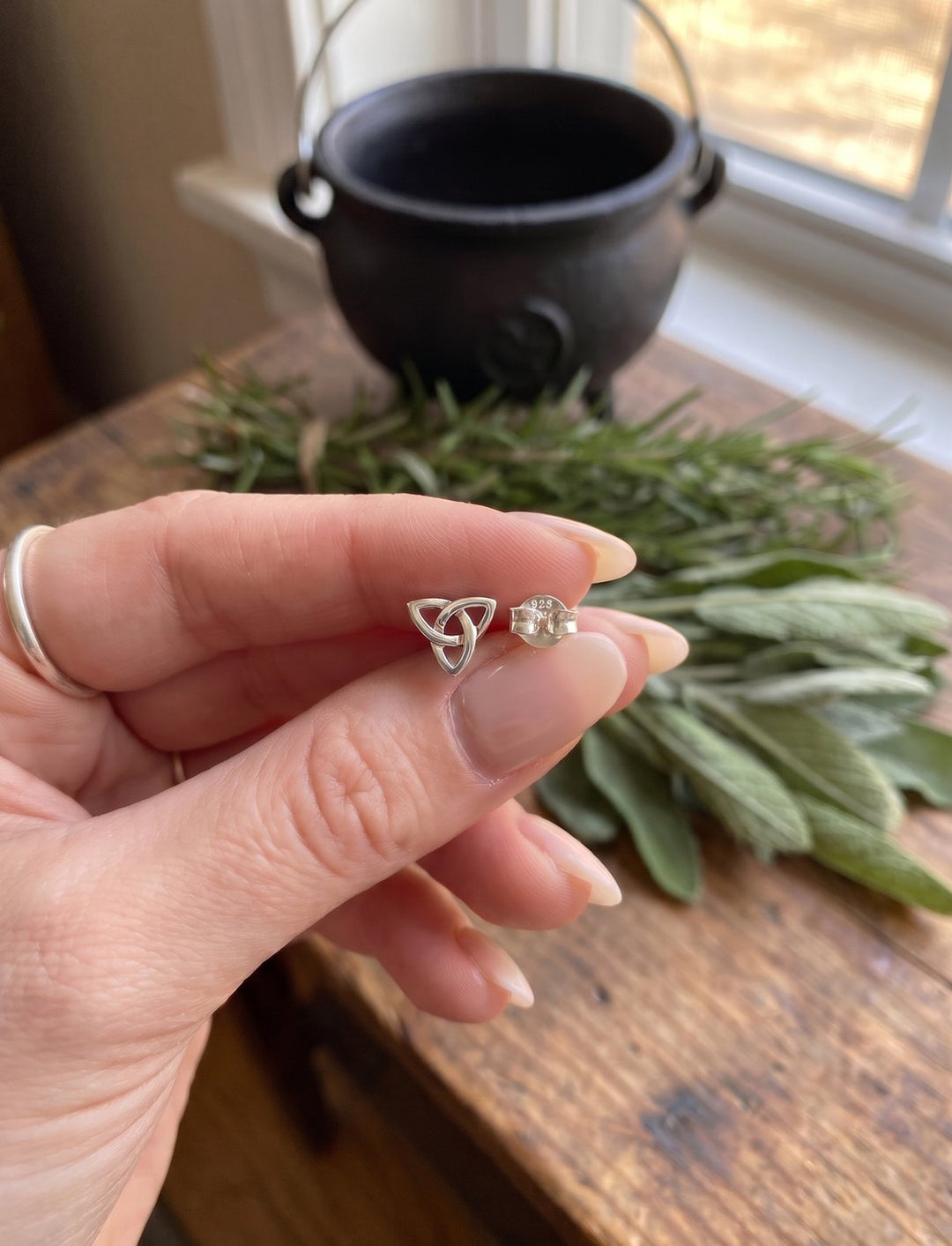Größenvergleich: Triquetra Ohrstecker ca. 7 × 8 mm mit 925 Ohrmutter zwischen Daumen und Zeigefinger