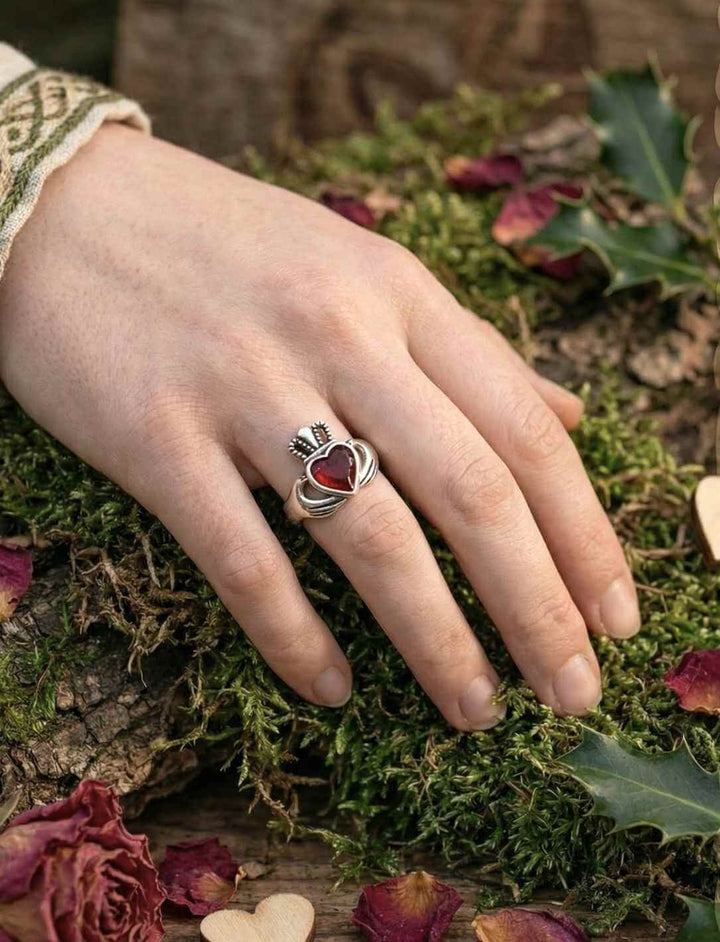 Claddagh Ring aus Silber mit rotem Zirkonia am Finger getragen in natürlicher Waldumgebung