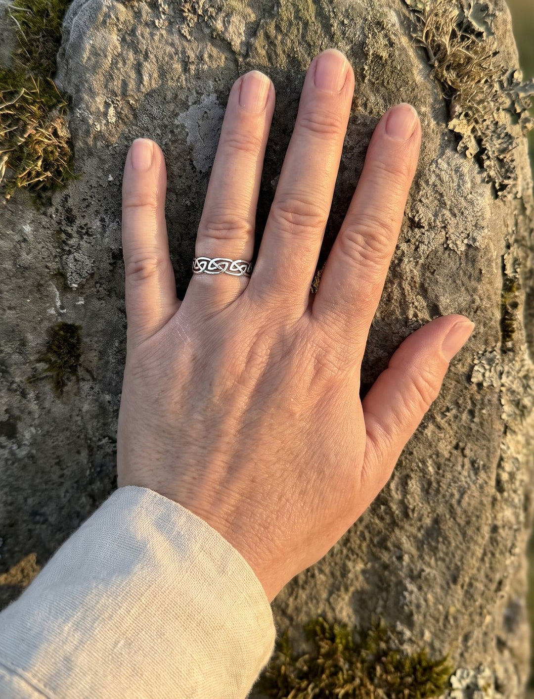 Größenvergleich: Frauenhand am alten Menhir trägt den 5 mm breiten keltischen Knotenring aus Silber am Ringfinger