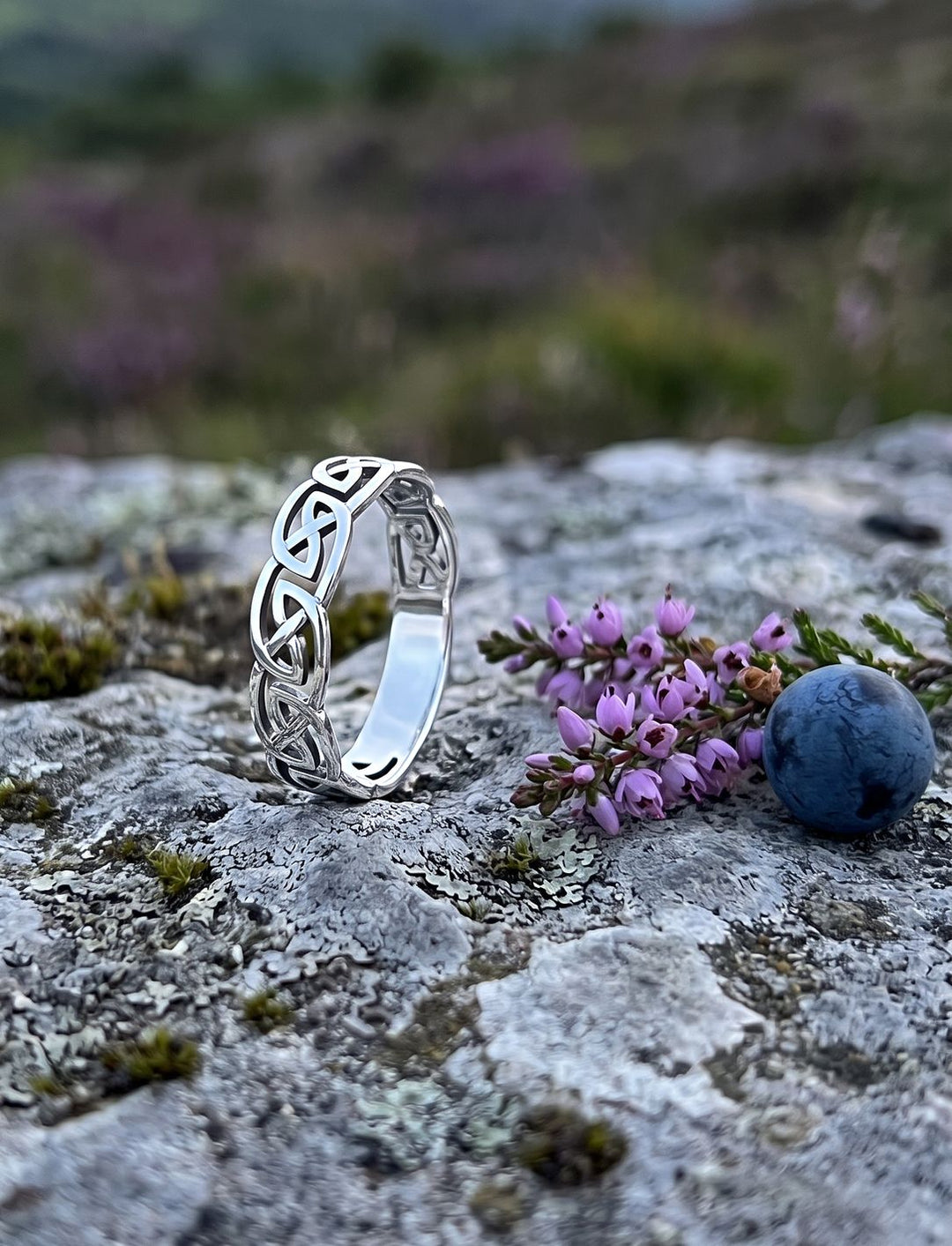 Durchbrochener Knotenring aus Sterling Silber auf Kalkstein mit lila Heidekraut und einer Schlehe im Abendlicht