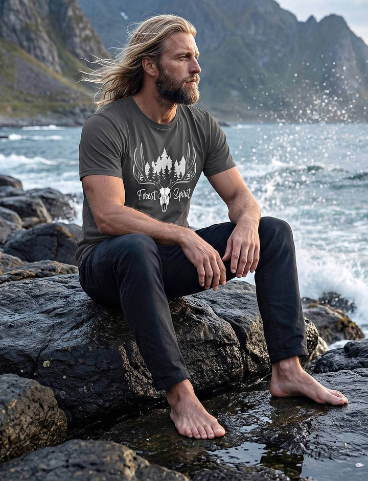 Herren T-Shirt in Anthrazit mit Geweih-Motiv, Mann sitzt barfuß auf Küstenfelsen vor Gischt und Bergen