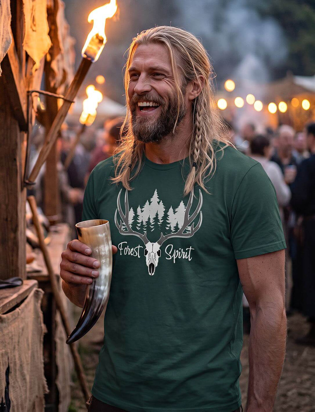 Lachender Mann im grünen Forest Spirit Shirt mit Trinkhorn auf einem abendlichen Mittelaltermarkt mit Fackeln