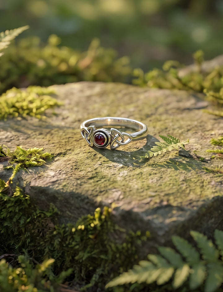 Glut von Bealtaine: Granat Ring aus Silber mit zwei Triquetras auf einem moosbewachsenen Stein im Wald