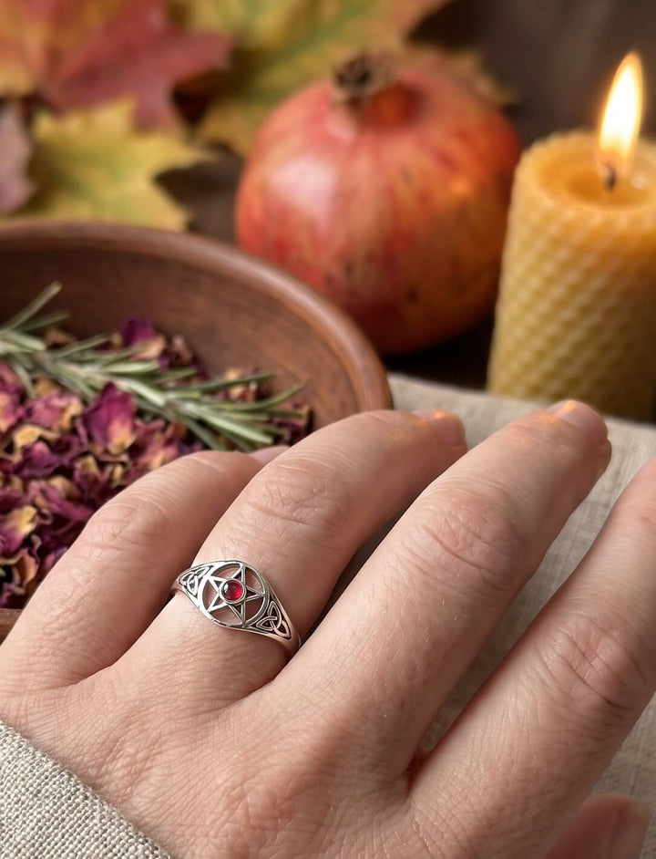 Silberner Drudenfuß-Ring mit Granatstein an der Hand, Samhain-Stimmung mit Rosenblüten, Granatapfel und Bienenwachskerze