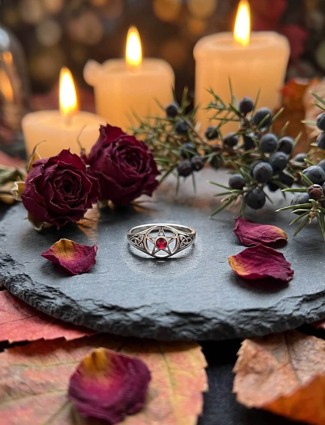 Glutstern der Triquetra: Pentagramm Ring aus Silber mit rotem Granat auf Schiefer zwischen Rosen, Wacholder und Kerzen