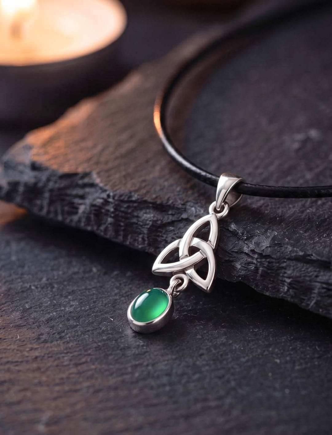 Grüner Achat Anhänger aus Silber mit keltischem Triquetra-Knoten auf dunklem Schiefer im Kerzenlicht