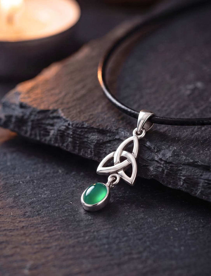 Grüner Achat Anhänger aus Silber mit keltischem Triquetra-Knoten auf dunklem Schiefer im Kerzenlicht
