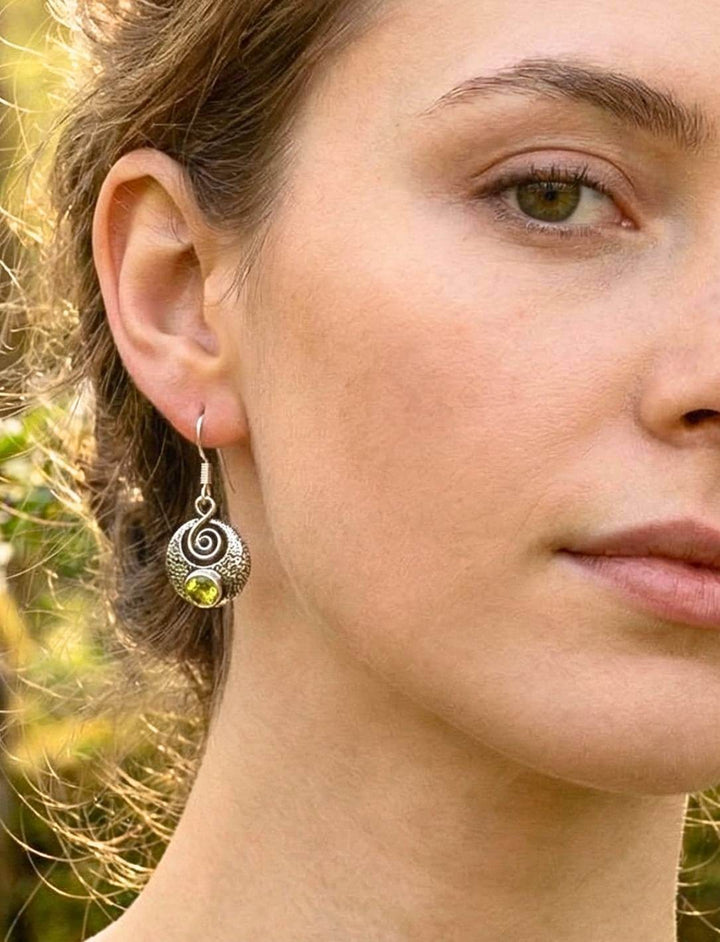 Frau trägt Silberohrring mit Peridot und Spirale Nahaufnahme im Waldlicht