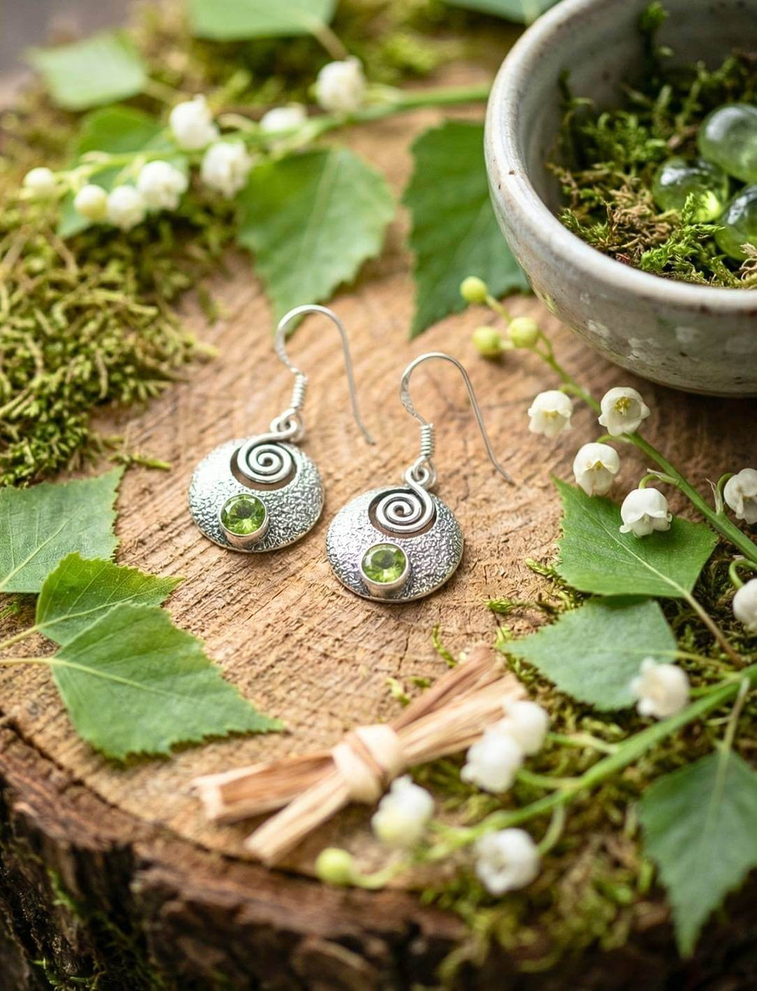 Silberohrringe mit Peridot auf Holzscheibe mit Maiglöckchen und Blättern