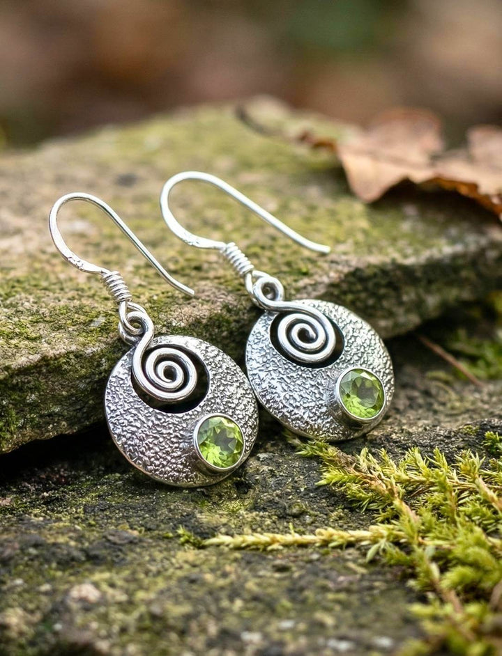 Keltische Ohrringe mit Peridot auf Schieferstein zwischen Moos und Herbstlaub