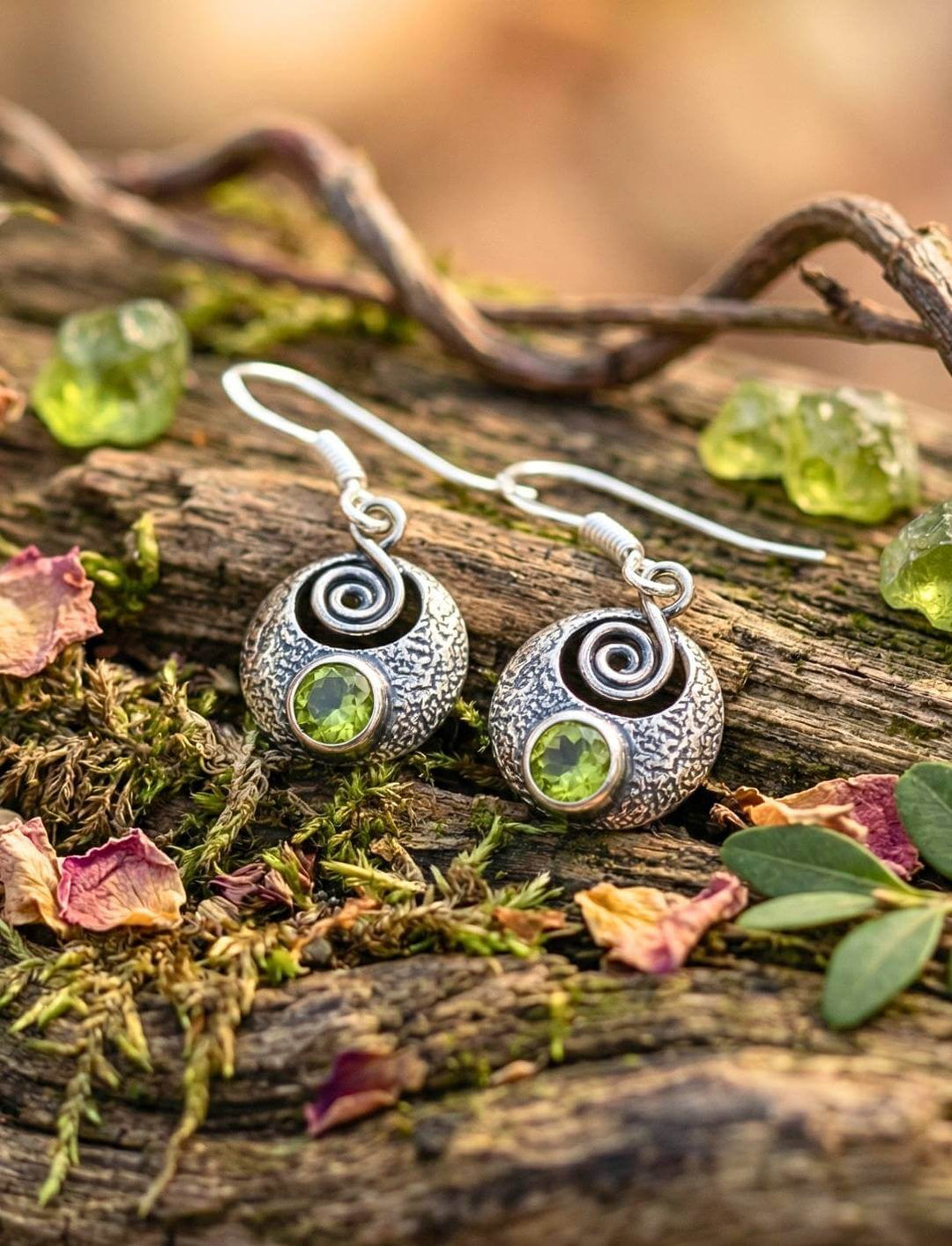 Silberohrringe mit grünem Peridot auf Holz und Zweigen