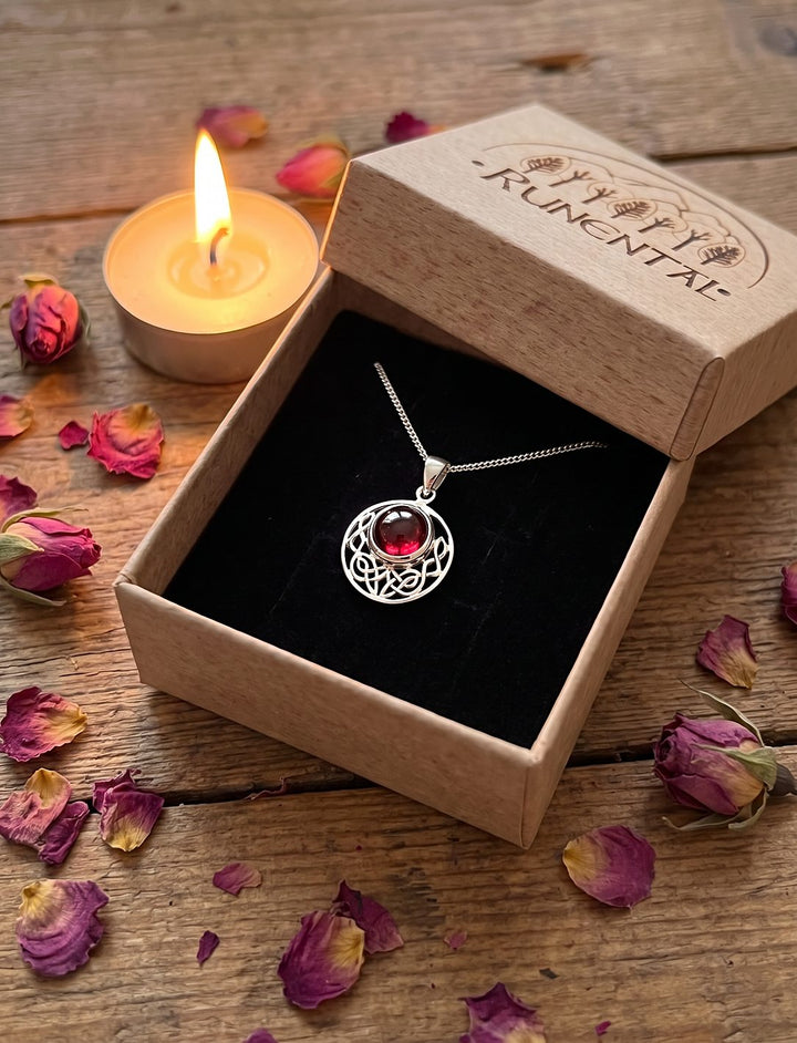 Runder Granat Silberanhänger an Silberkette in der Runental Geschenkbox neben Teelicht und getrockneten Rosen