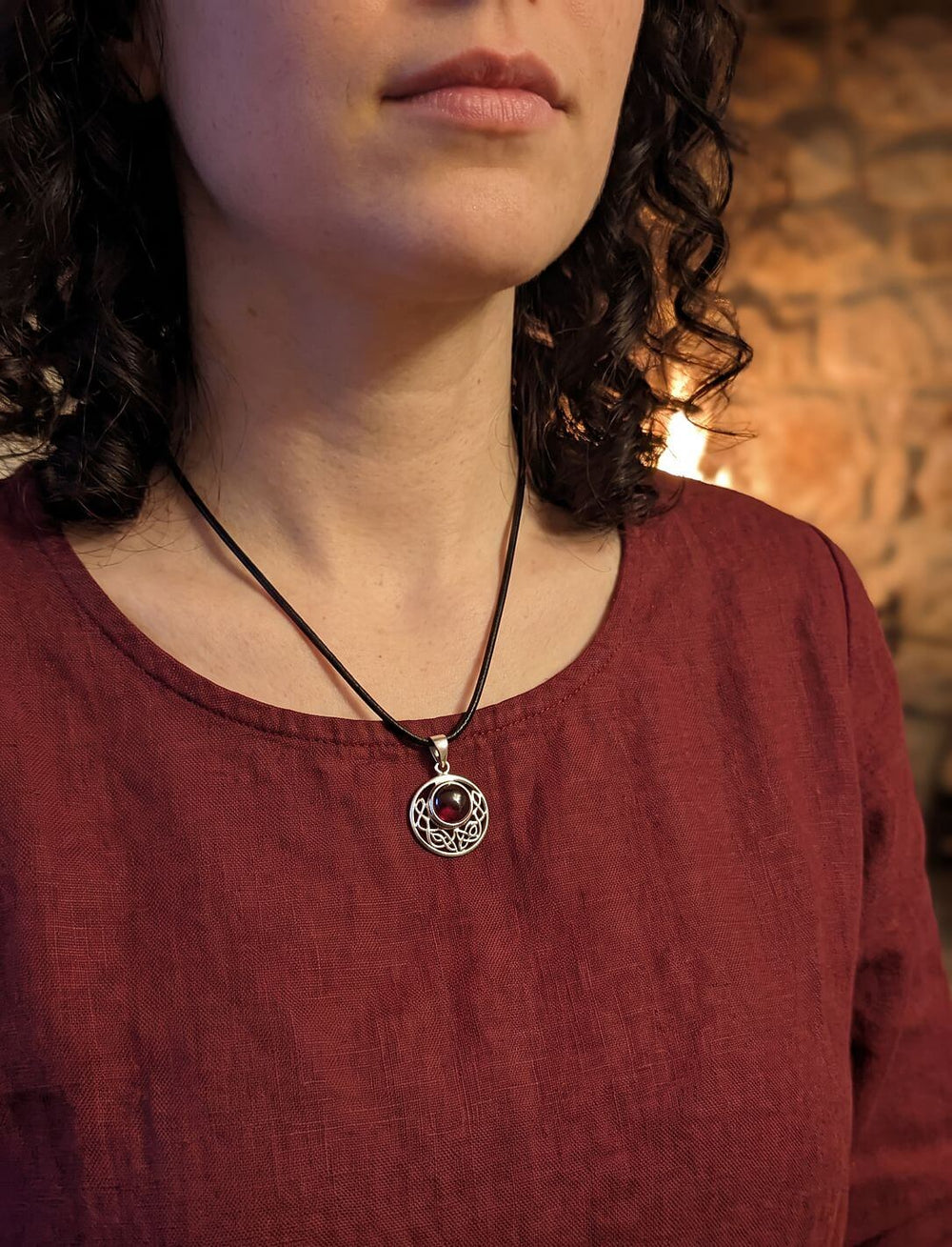 Frau im dunkelroten Leinenshirt trägt den keltischen Knoten Anhänger mit Granat an schwarzer Lederkette am Kamin