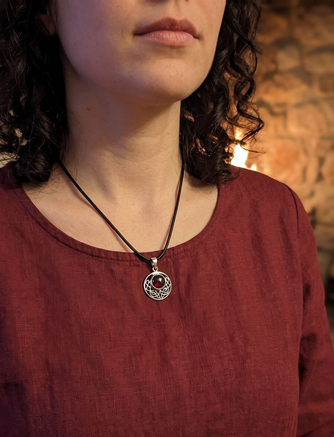 Frau im dunkelroten Leinenshirt trägt den keltischen Knoten Anhänger mit Granat an schwarzer Lederkette am Kamin