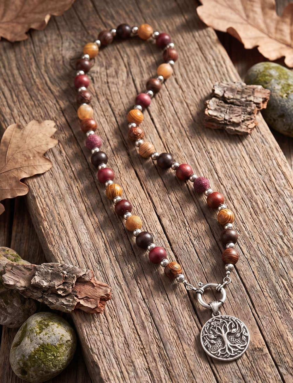Kette aus braunen und roten Holzperlen auf verwittertem Holz mit Herbstlaub und Steinen