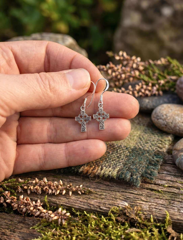 Hand zeigt Größe der Keltenkreuz Silber Ohrhänger über Heidekraut und Stein