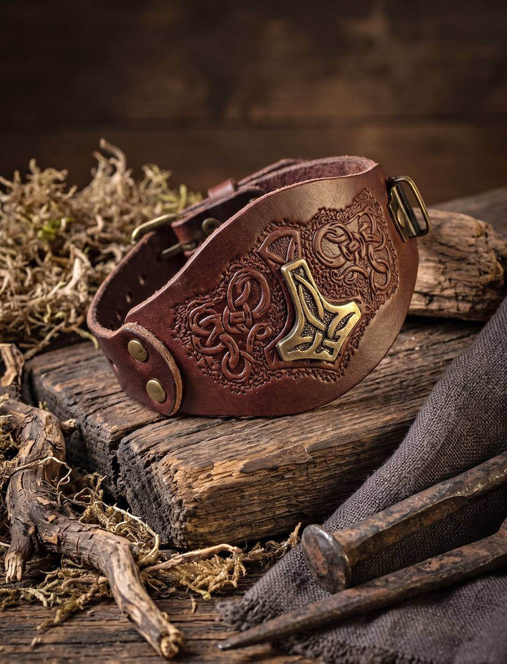 Braunes geprägtes Lederarmband mit Thorshammer-Beschlag, aufgestellt auf altem Holz zwischen Moos und Wurzeln