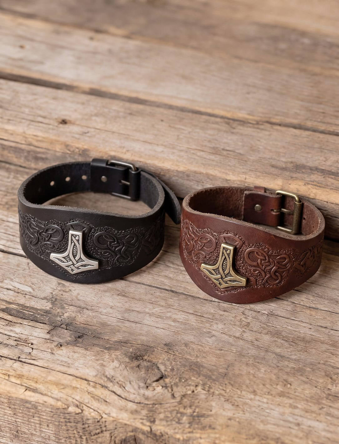 Thors Hammer Armband in Schwarz mit silberfarbenem und in Braun mit messingfarbenem Hammer nebeneinander auf Holz