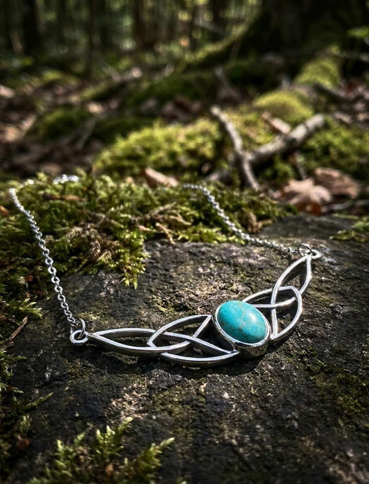 Keltischer Knoten-Charm mit türkisem Cabochon auf bemostem Stein