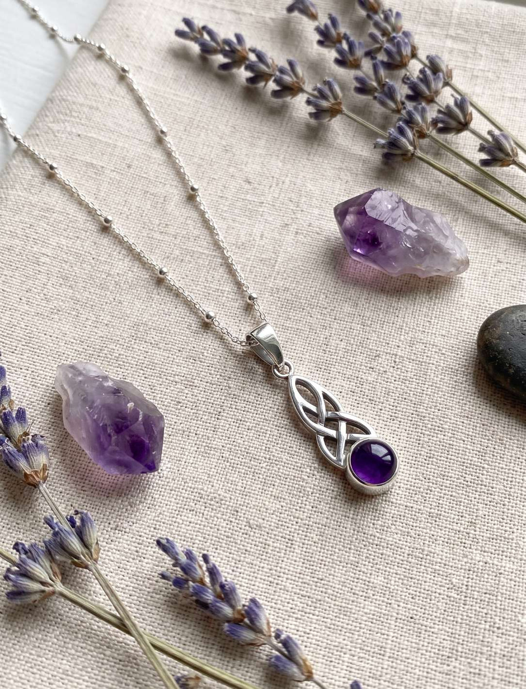 Silberanhänger mit Amethyst neben Rohamethyst und getrocknetem Lavendel auf Leinenstoff