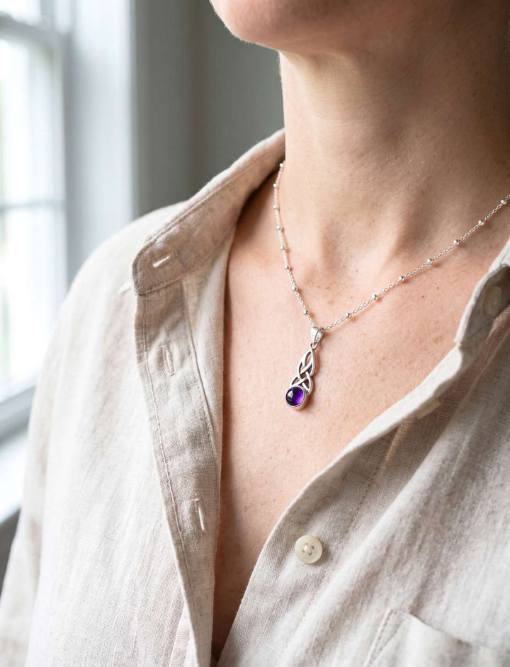 Frau trägt filigranen Silberanhänger mit violettem Amethyst an feiner Kugelkette zu offenem Leinenhemd