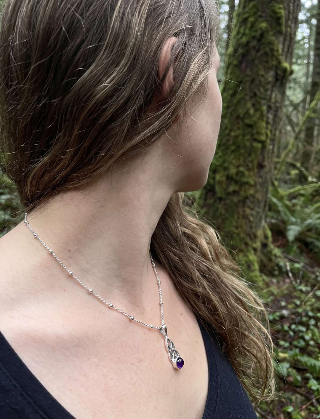 Frau im Wald trägt keltischen Silberanhänger mit Amethyst am Schlüsselbein, Seitenansicht
