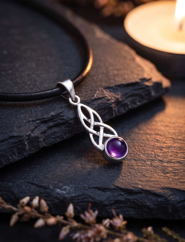 Keltischer Knoten Anhänger mit Amethyst an schwarzem Lederband auf dunklem Schiefer im Kerzenlicht