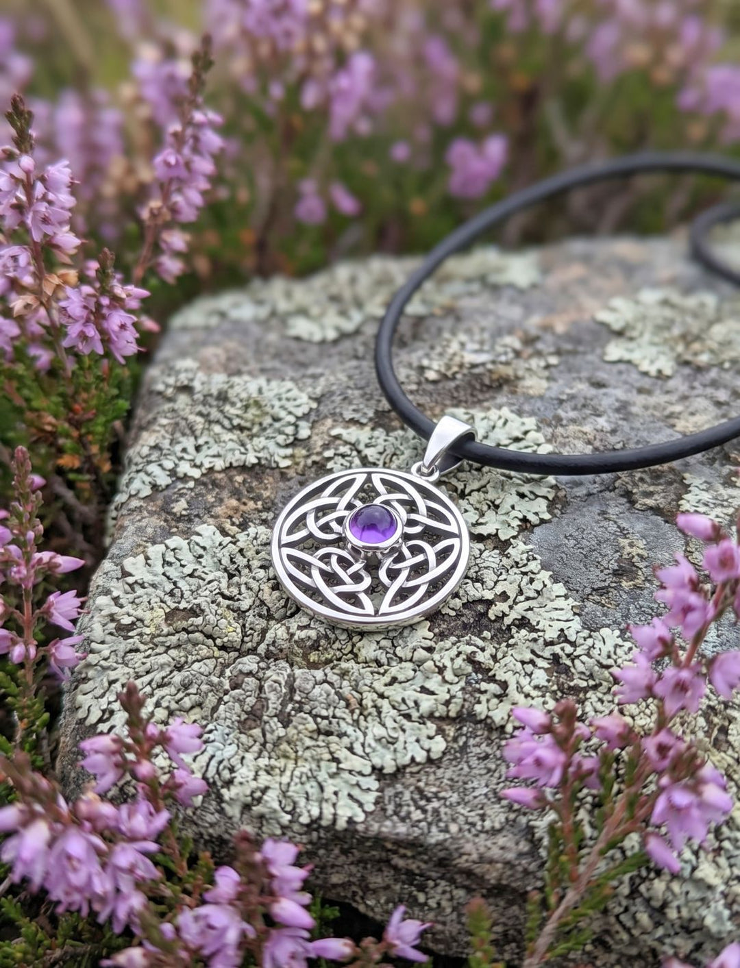 Keltischer Silber Anhänger mit Amethyst an schwarzer Kordel auf Flechtenstein zwischen blühender Heide