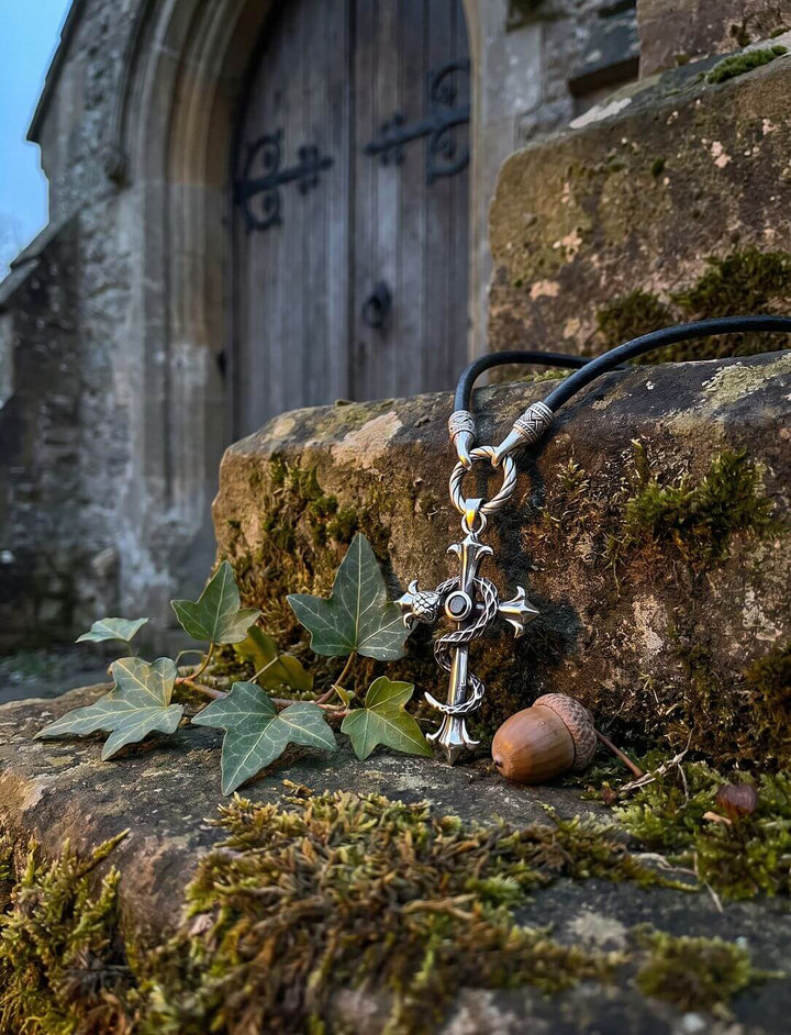 Kreuzanhänger mit Lilienenden am Band des Hüters auf moosiger Steinmauer vor alter Kirchentür, mit Efeu und Eichel